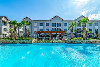 A large swimming pool in front of a building with a balcony and palm trees.